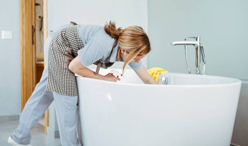 Woman scrubbing bathtub inside bathroom