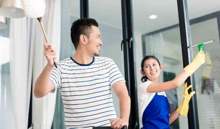 Woman in blue-white dress cleaning glass and man is cleaning light fixture.