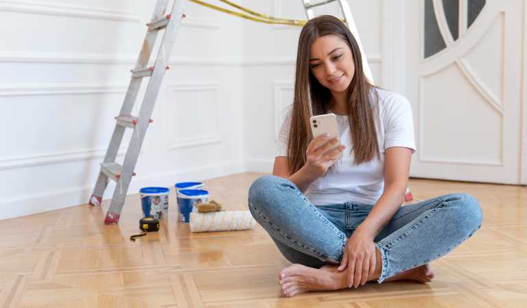 Woman in white t-shirt and blue jeans sitting on floor and using her mobile.