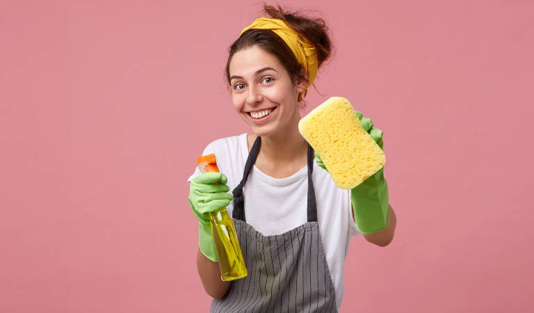 Woman in green gloves holding a spray bottle and scrubber in her hand.