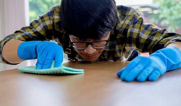 Man in check shirt and blue gloves cleaning a table with a cloth