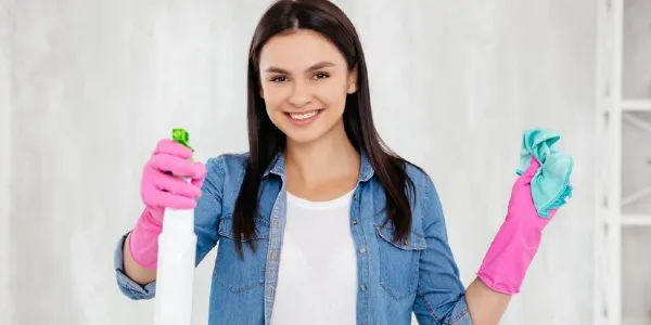 Woman in blue shirt and pink gloves holding a white bottle and a blue cloth in her hand.
