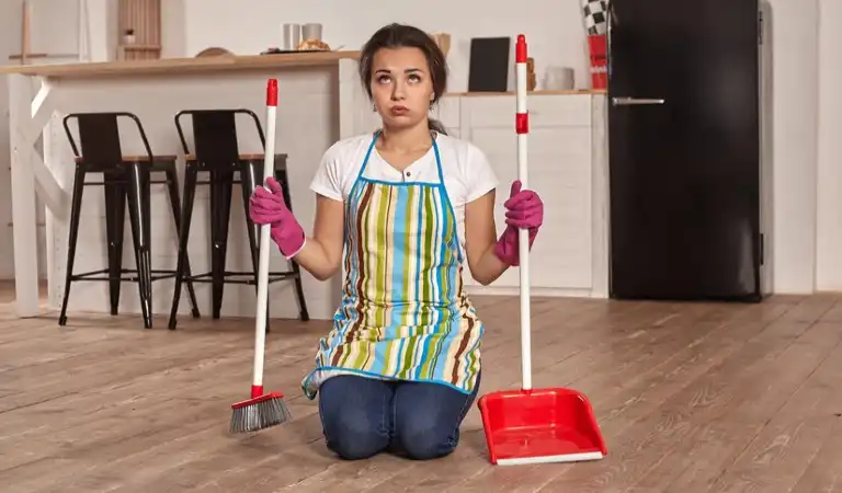 A lady sitting on floor on her knees holding two cleaning sticks in her hand.