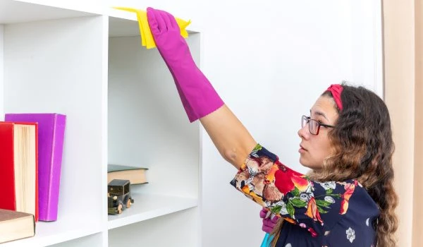 woman in rubber gloves cleaning white shelves