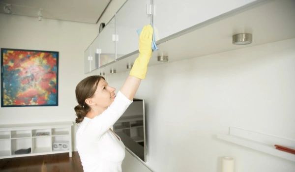 Young woman cleaning an upper surface of the shelf