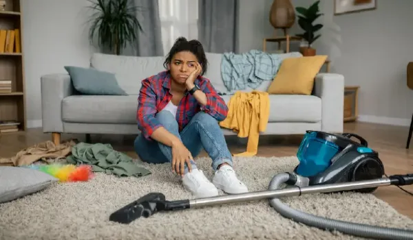 Unhappy tired female sit on floor with vacuum cleaner