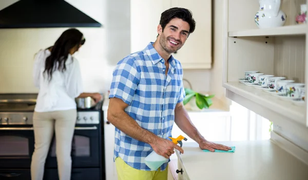 Man cleaning the kitchen and woman cooking food in background
