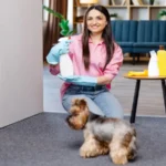 Young woman sitting near the table with cleaning products at home and her little dog is running next to her