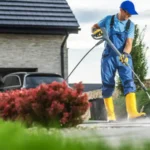 Man using a pressure washer to clean driveway while standing on a sunny afternoon