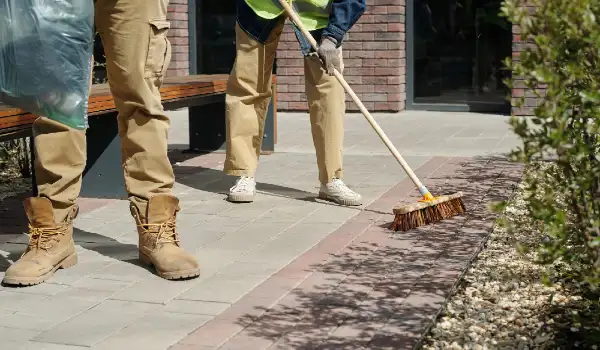 Two young adult men sweeping outdoor pavement during daytime cleanup