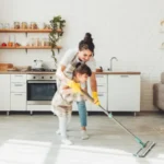 A little daughter and her mom clean the house a child washes the kitchen floor a cute little helper girl cleans the floor with a mop a happy family cleans the room