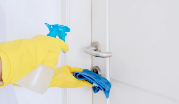 Hands cleaning door handle with disinfectant spray