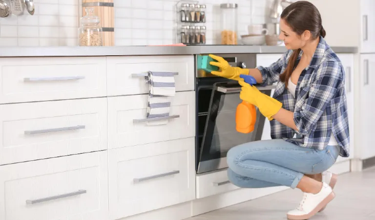 Young woman cleaning oven in kitchen